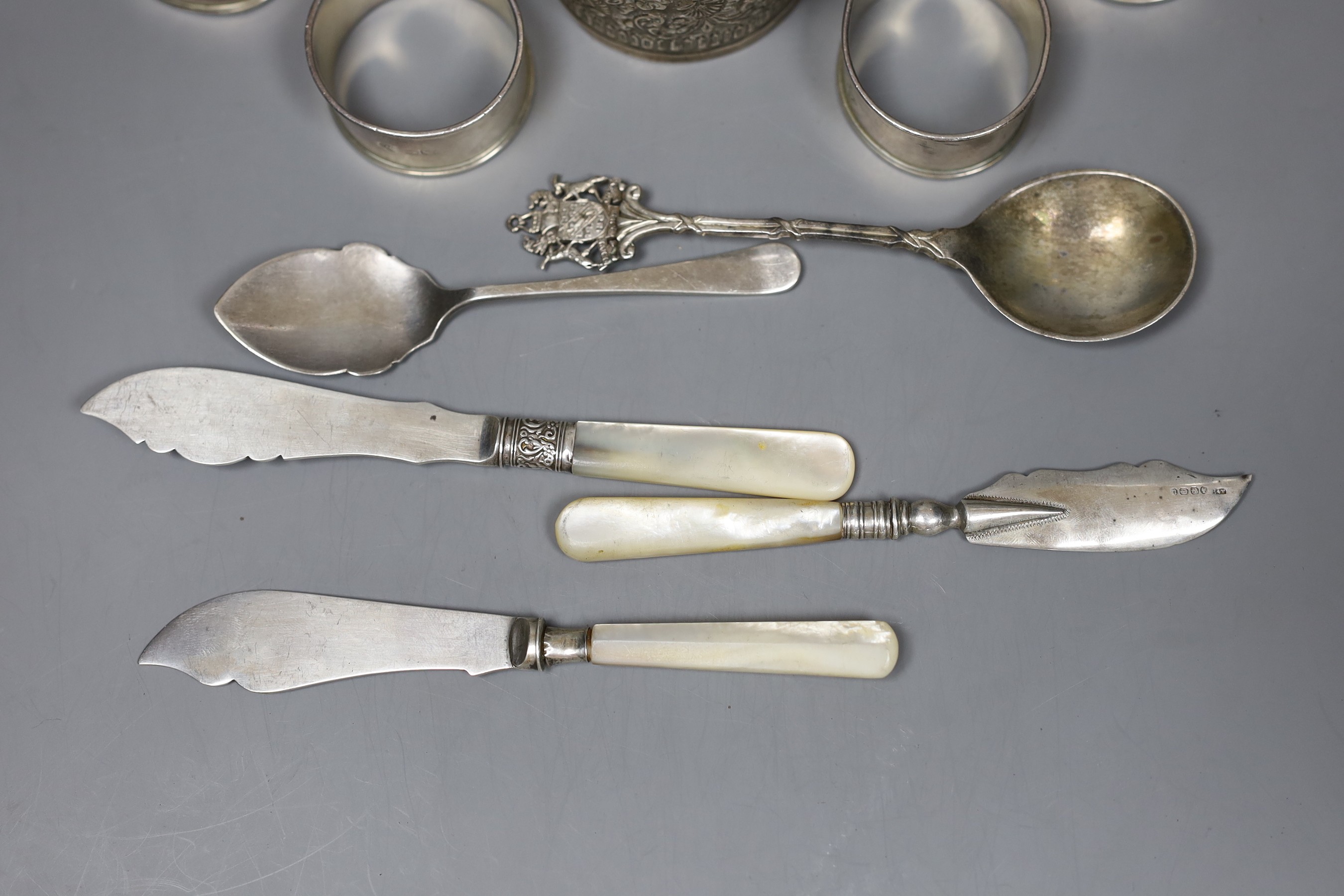 A 19th century Indian white metal christening can with cobra handle, a set of four silver napkin rings, two spoons and three mother of pearl handled butter knives.